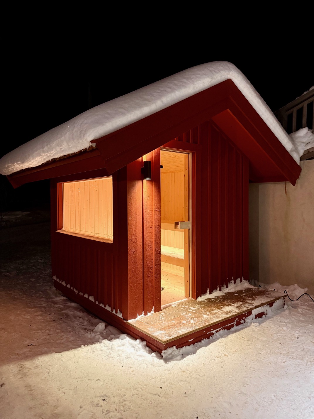 Nybyggd röd bastu i vintermiljö med varmt ljus inifrån